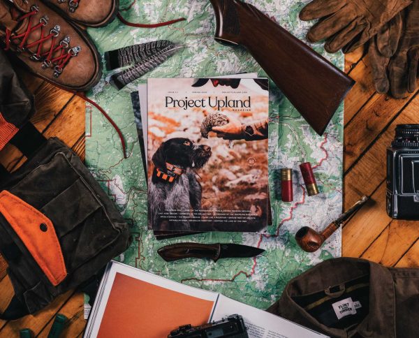 A stack of Project Upland Magazines with hunting gear