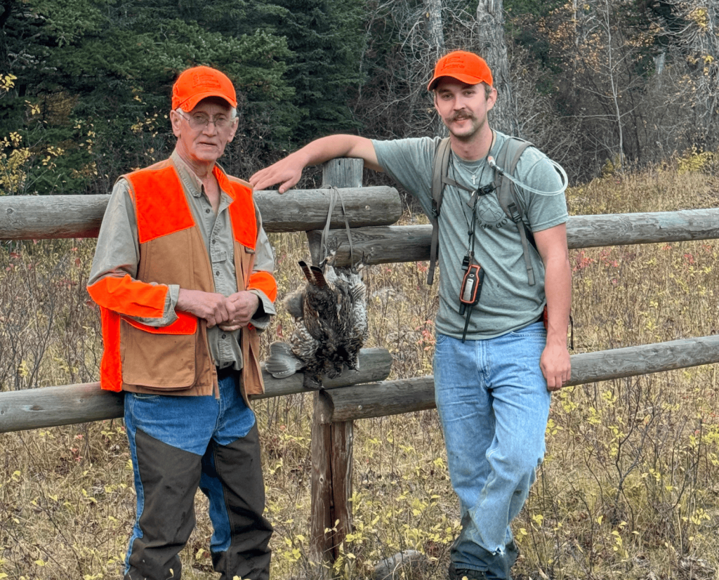 The author and his grandfather standing along a wooden fence with two dead ruffed grouse.