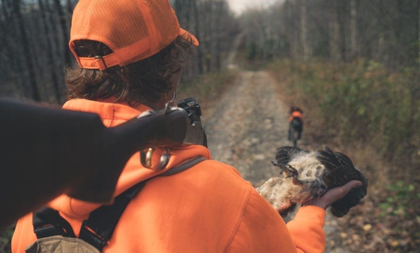 A bird hunter with her hunting dog and a ruffed grouse in Maine