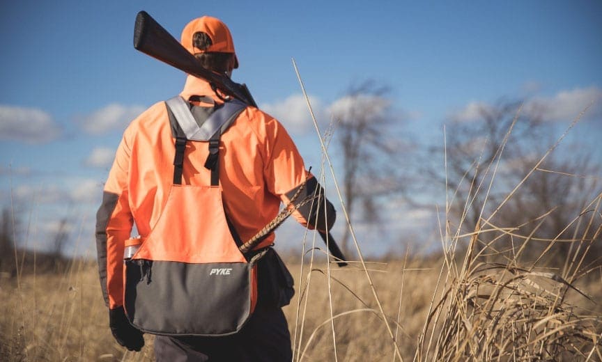 A hunter walks in a field with a pyke vest on. 